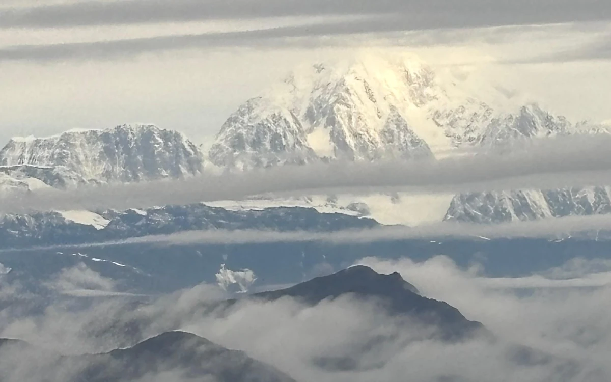 The summit of Denali rising above a layer of cloud, seen from a small aircraft flying along the range