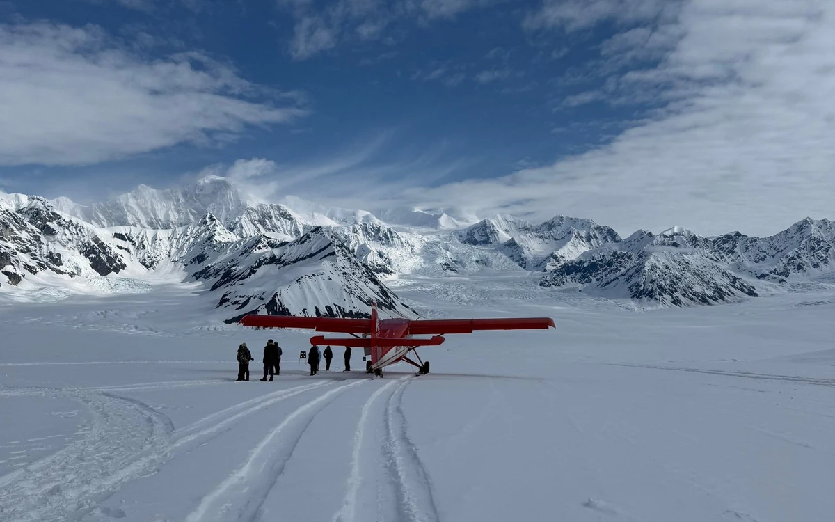 A red ski plane standing on packed snow with granite peaks behind it