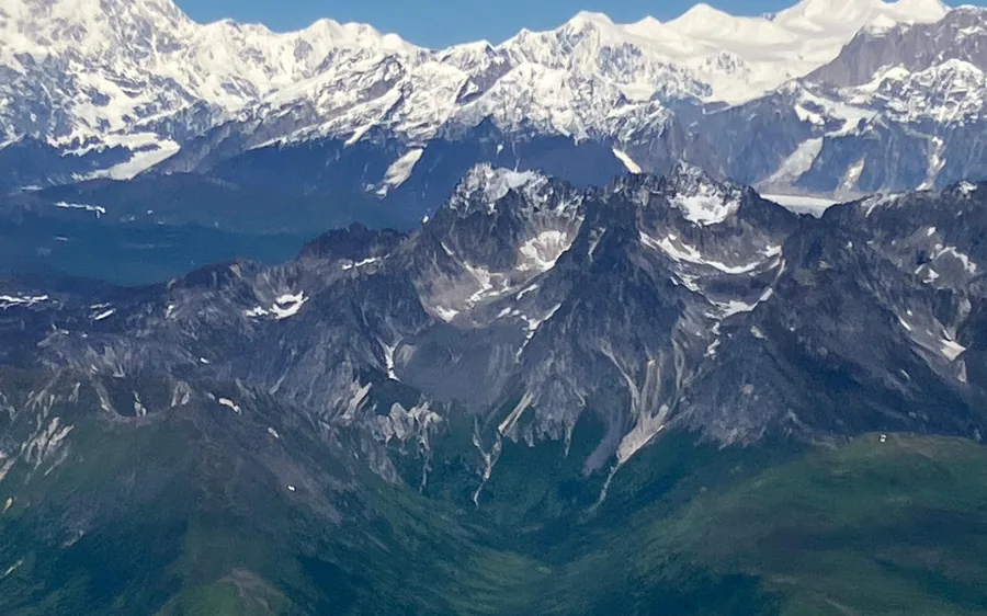 Dark green ridges below the snow peaks of the Alaska Range seen from a plane