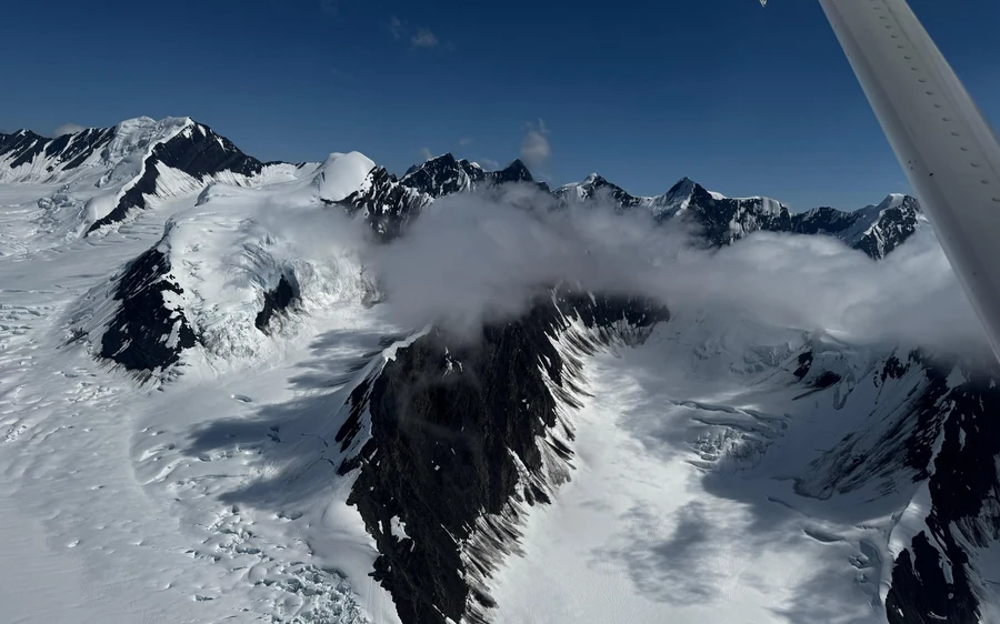 Snow-covered peaks and glaciers seen from a small plane with the wing strut in the top corner